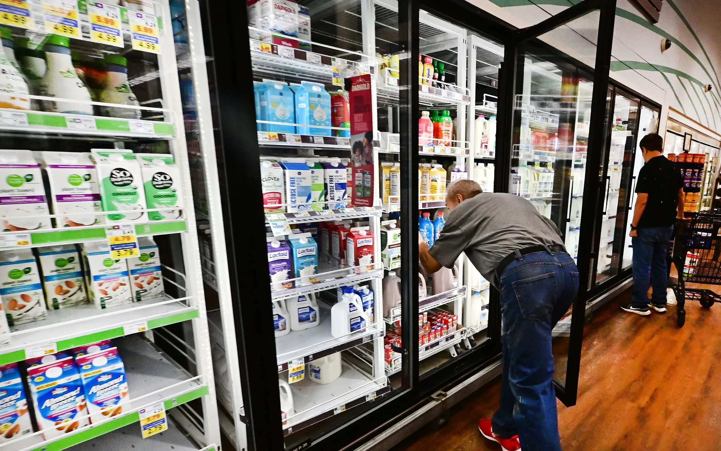 رجال يتسوقون في متجر، يختارون منتجات الألبان من الثلاجات، في سياق ارتفاع أسعار المواد الغذائية.