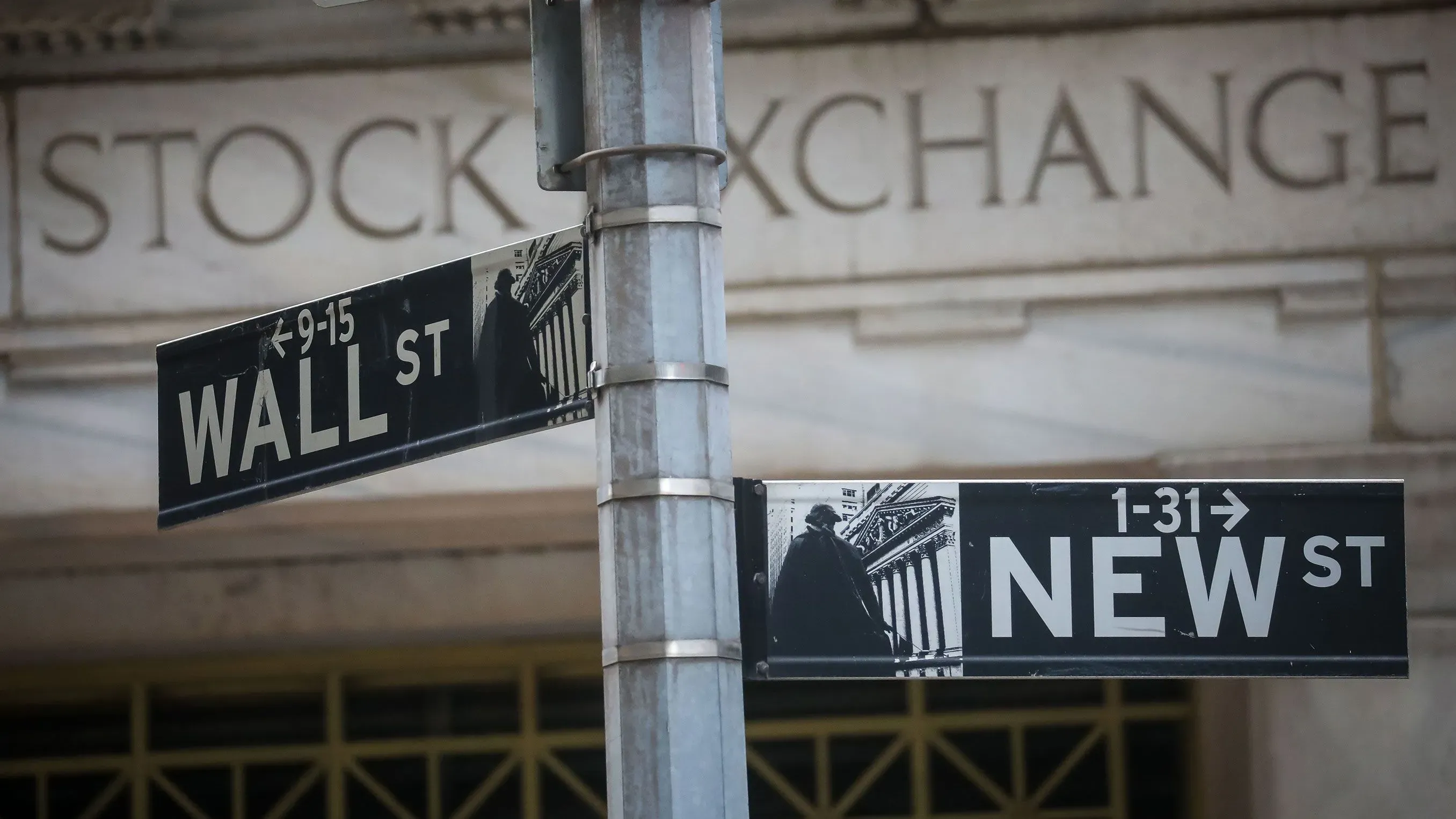 لافتة تشير إلى تقاطع شارع وول ستريت وشارع نيو، مع خلفية مبنى بورصة نيويورك، تعكس النشاط الاقتصادي في وول ستريت.