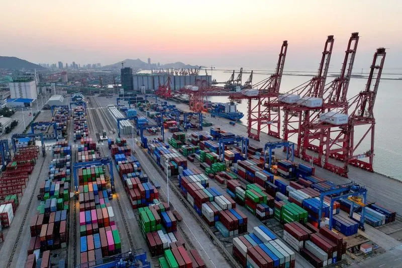 صورة لميناء شحن مزدحم يظهر فيه حاويات ملونة تتكدس على الأرصفة، مع رافعات تعمل في الخلفية، مما يعكس نشاط التجارة بين الولايات المتحدة والصين.