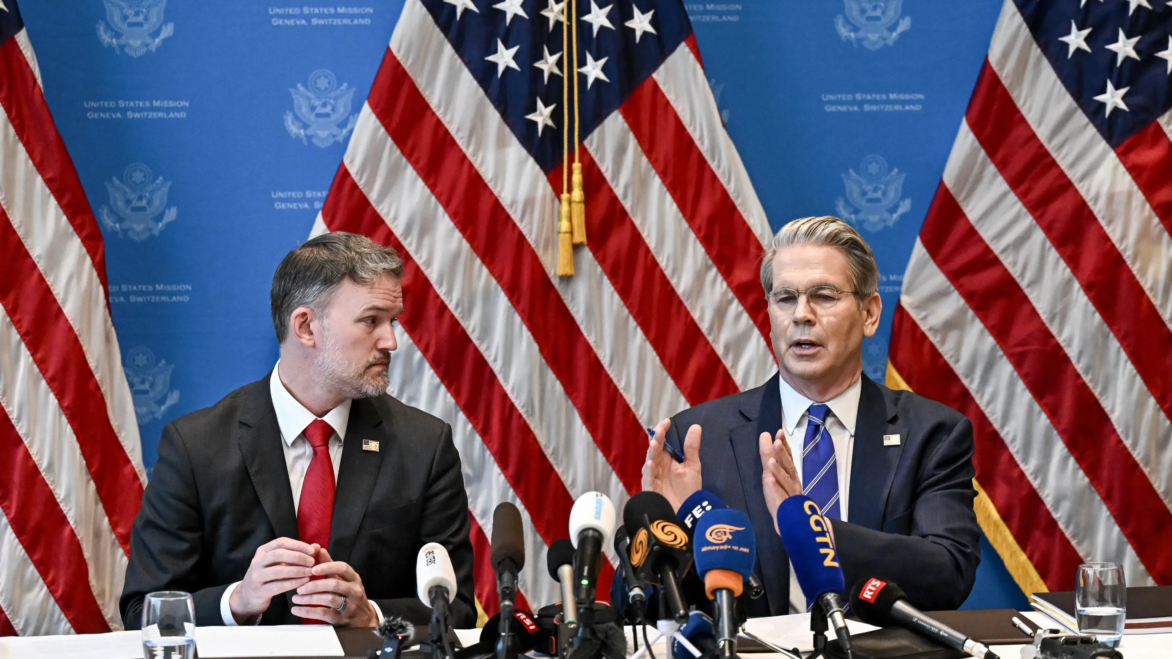اجتماع بين مسؤولين أمريكيين في جنيف، مع أعلام الولايات المتحدة خلفهم، حيث يتناولون تخفيف التوترات التجارية مع الصين.