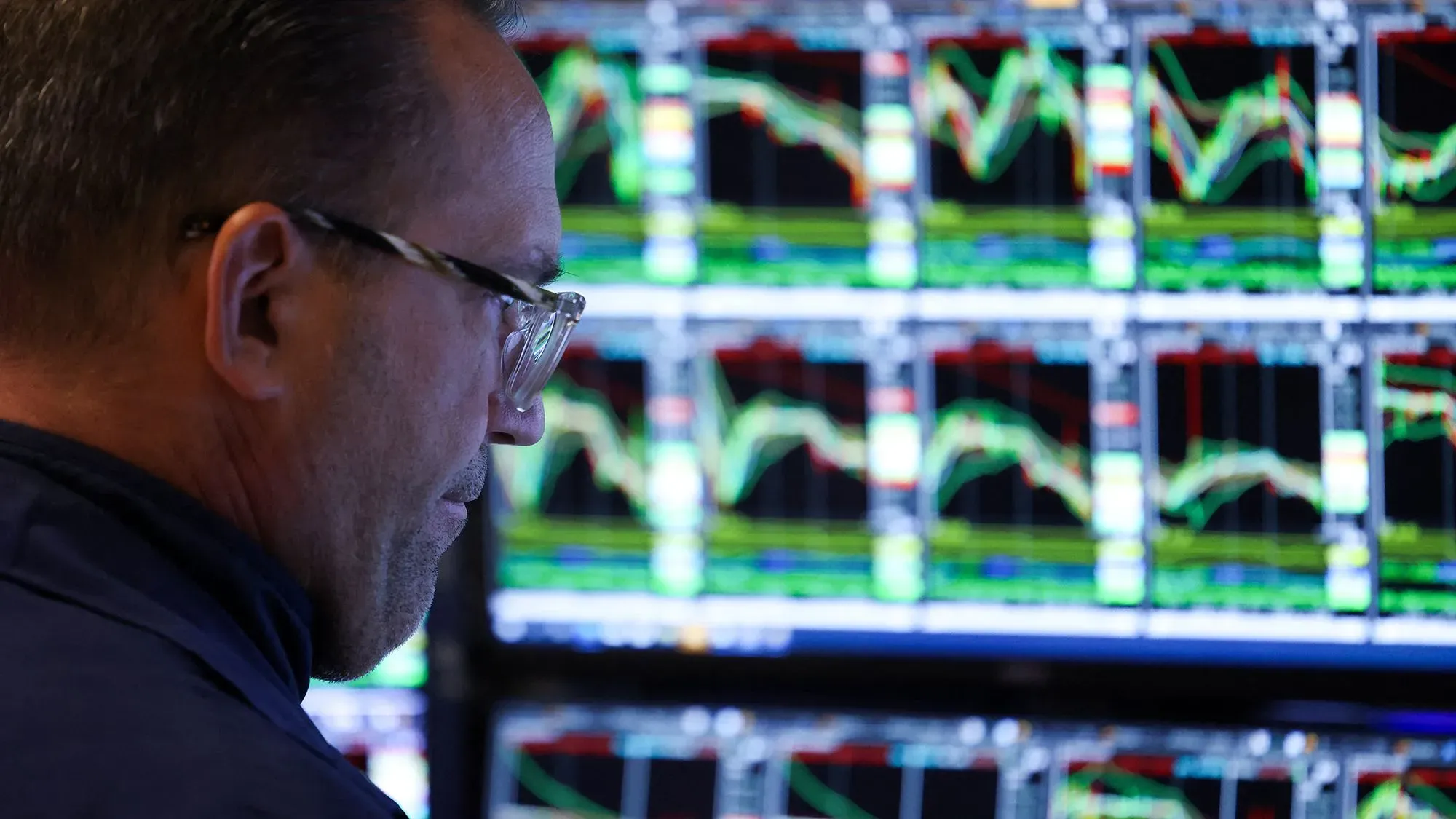 تاجر يتابع تحركات الأسهم على شاشات متعددة، في ظل تراجع السوق الأمريكي بسبب تهديدات ترامب بفرض رسوم جديدة.