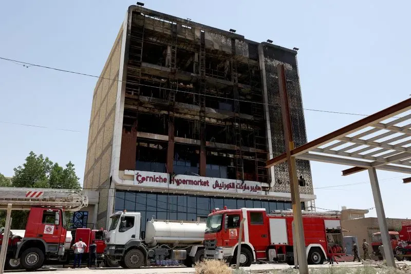 مبنى هايبر ماركت الكورنيش المتضرر من حريق هائل في الكوت، مع وجود سيارات إطفاء في الموقع بعد جهود الإنقاذ.
