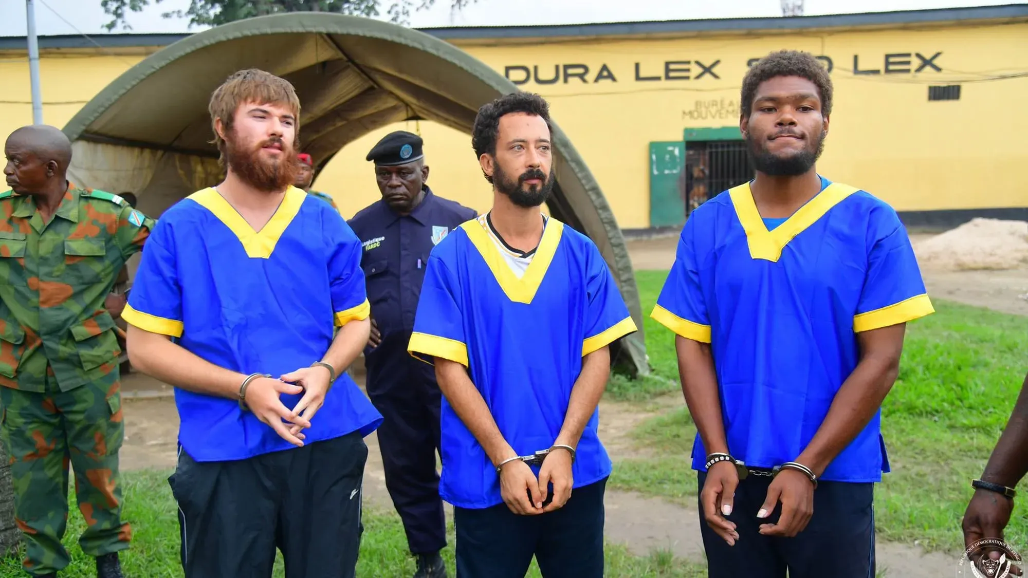 ثلاثة أمريكيين يرتدون ملابس زرقاء، يقفون مع ضباط أمن في جمهورية الكونغو الديمقراطية، بعد تخفيف أحكام الإعدام بحقهم.