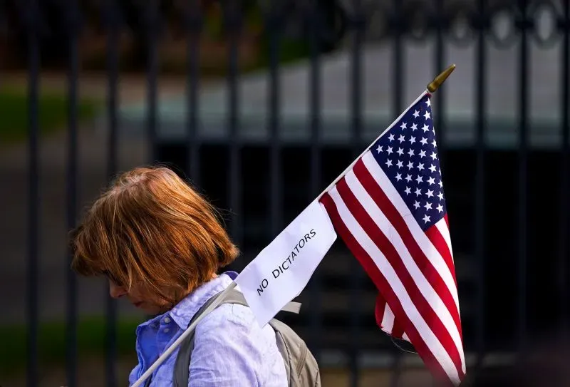 امرأة تحمل علم الولايات المتحدة مع لافتة مكتوب عليها "لا للديكتاتوريين"، تعبر عن موقفها السياسي في تظاهرة.