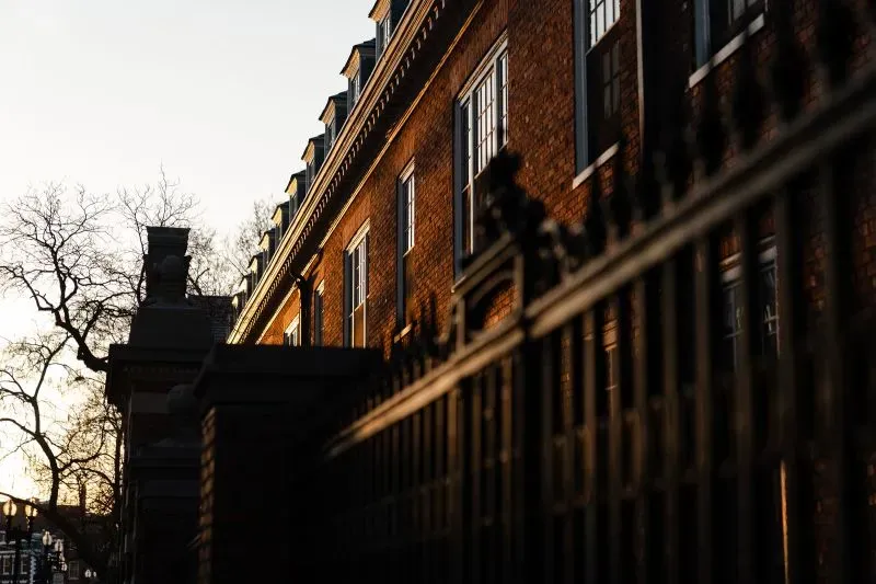 واجهة مبنى جامعي تاريخي في الولايات المتحدة، مع أشجار عارية في الخلفية وأشعة الشمس تغمر المكان، تعكس القلق بشأن مستقبل الطلاب الصينيين.