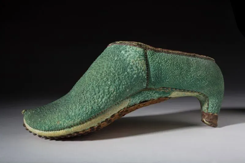 حذاء بكعب عالٍ باللون الأخضر، يظهر تصميمه الفريد وتفاصيله الدقيقة، يعكس تاريخ الأحذية ذات الكعب العالي وتأثيرها عبر العصور.