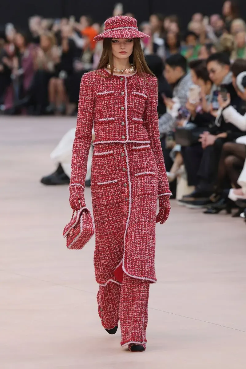 فستان أنيق باللون الأحمر مع جيوب بارزة، يعكس تصميم شانيل في عرض أزياء ميت غالا 2023، مع حضور لافت من الجمهور.