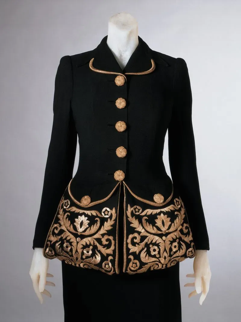 جاكيت أسود مزين بتطريز ذهبي، يتميز بأزرار بارزة وجيوب كبيرة، يعكس تصميمه التاريخي واهتمام الموضة بالجيوب في الملابس النسائية.