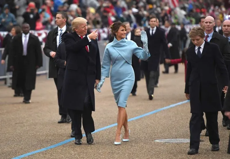 ميلانيا ترامب ترتدي فستانًا أزرق مع بعض التفاصيل الفريدة، وتمشي بجانب دونالد ترامب وسط حشد من المواطنين في حفل تنصيب.