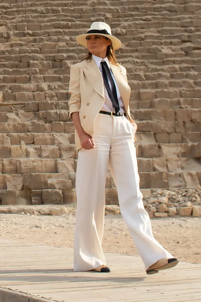 ميلانيا ترامب ترتدي بدلة أنيقة ذات لون فاتح مع قبعة، أمام هرم في مصر. تعكس إطلالتها أسلوبها الأوروبي الفاخر.