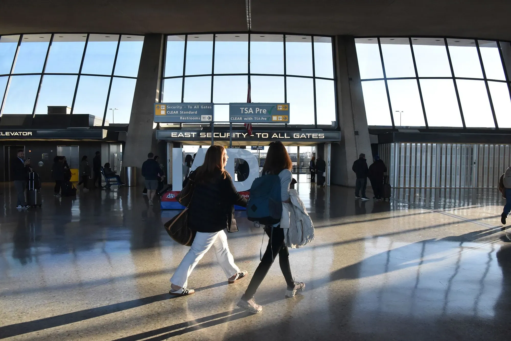 مشهد داخلي لمطار دالاس الدولي يظهر الركاب وهم يسيرون نحو بوابات الطائرات، مع لافتات توجيهية واضحة، تعكس ازدحام المطار.