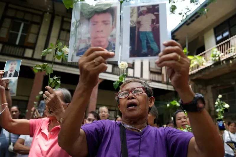 امرأة تحمل صورًا لأحباء مفقودين خلال احتجاج على جرائم الحرب في الفلبين، مع تعبير عن الألم والأمل في العدالة.