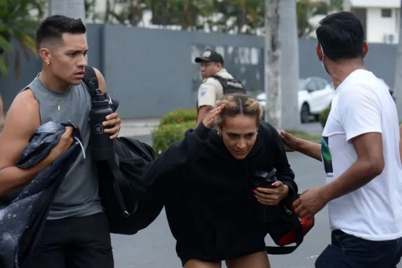 مواطنون إكوادوريون يهرعون في الشارع خلال حالة طوارئ، مع وجود رجال الشرطة في الخلفية، في سياق انتخابات رئاسية وسط أزمة أمنية.