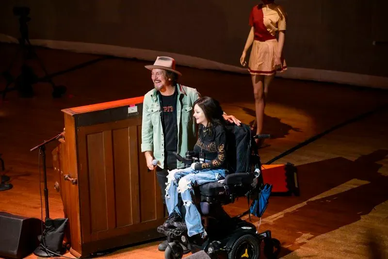 إيدي فيدر مع فتاة تستخدم كرسيًا متحركًا على خشبة المسرح، خلال حفل لجمع التبرعات لمؤسسة أبحاث انحلال البشرة الفقاعي.