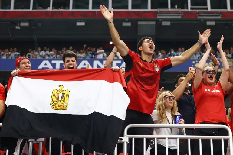مشجعون مصريون يرفعون علم مصر ويهتفون بحماس في مدرجات كأس العالم لدعم منتخب الفراعنة خلال مباراة مثيرة.