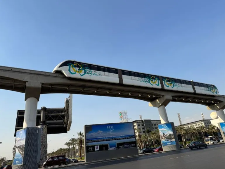 مونوريل شرق النيل يسير فوق شوارع القاهرة، مع إعلانات تجارية في الأسفل، ويظهر كوسيلة نقل حديثة تربط المناطق المختلفة.