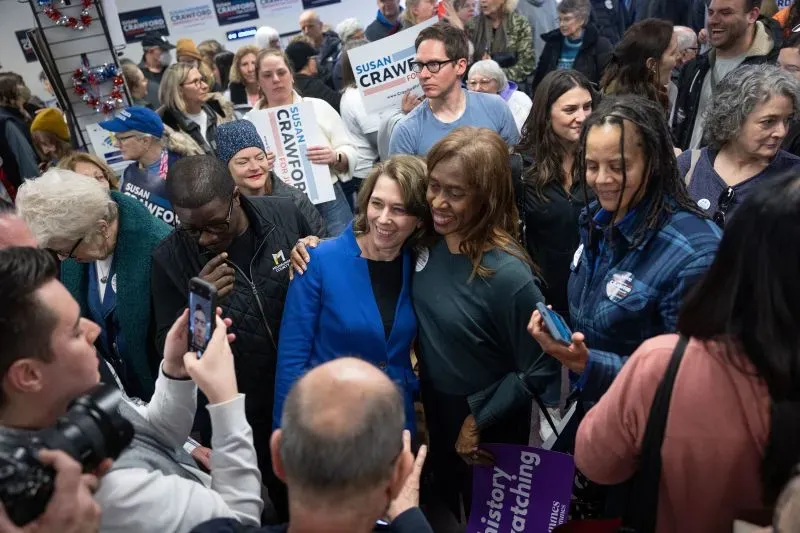 حشد كبير من مؤيدي سوزان كروفورد في قاعة بلدية، حيث تتوسطها كروفورد وهي تبتسم مع أحد الحضور، في إطار فعاليات الحملة الانتخابية.