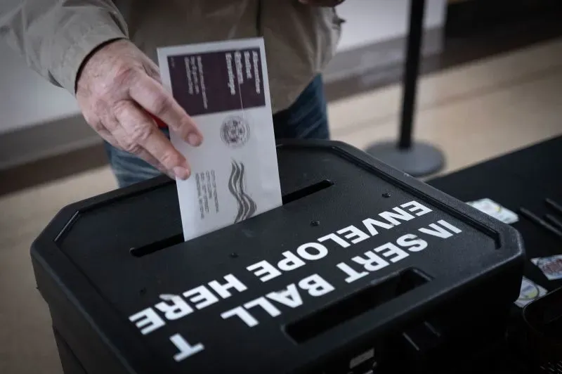 ناخب يضع بطاقته الانتخابية في صندوق الاقتراع، مع وجود علامة واضحة تشير إلى مكان الإدلاء بالأصوات، خلال السباق الانتخابي في ويسكونسن.