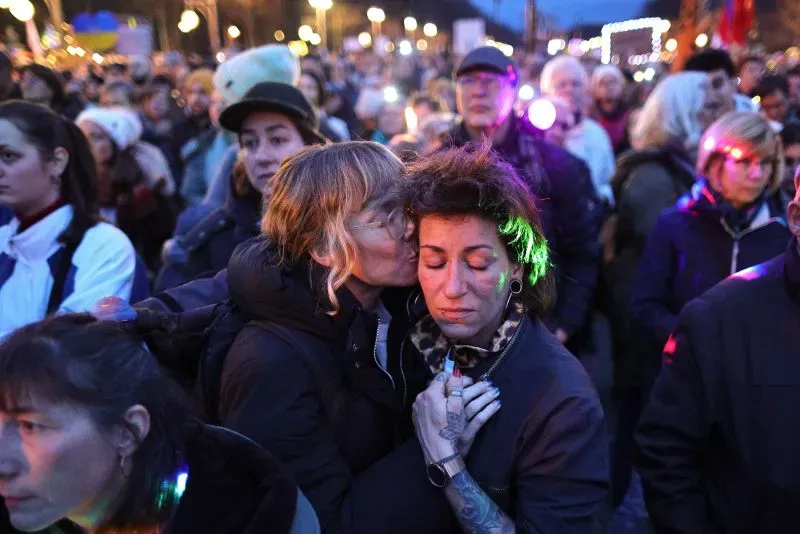 امرأتان في حشد من المتظاهرين، واحدة تحتضن الأخرى وتقبل جبهتها، تعبيرًا عن الدعم في وقت احتجاج على حزب البديل في ألمانيا.