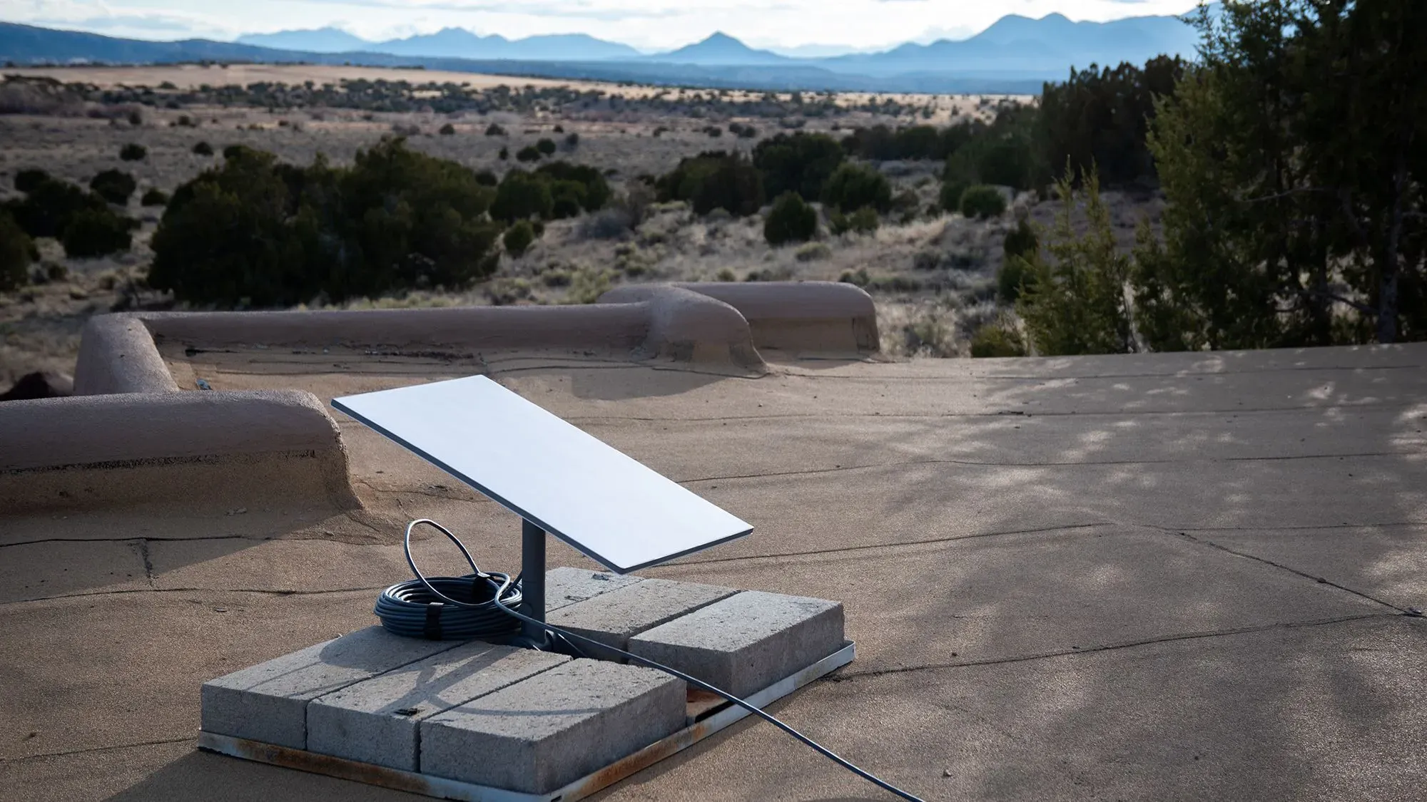 جهاز استقبال Starlink مثبت على سطح، مع منظر طبيعي واسع في الخلفية، يمثل خدمة الإنترنت عبر الأقمار الصناعية.