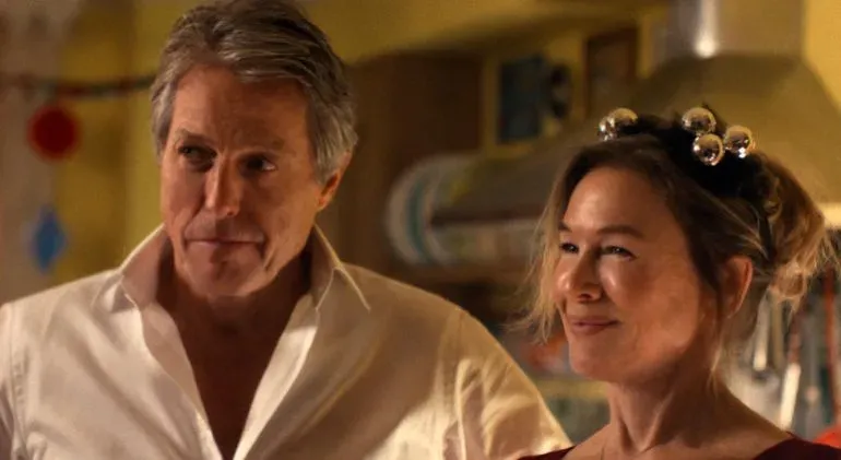 لقطة لممثلين يتحدثان معاً في مشهد درامي، يعكسان تفاعلاً حميمياً في إطار احتفالي.