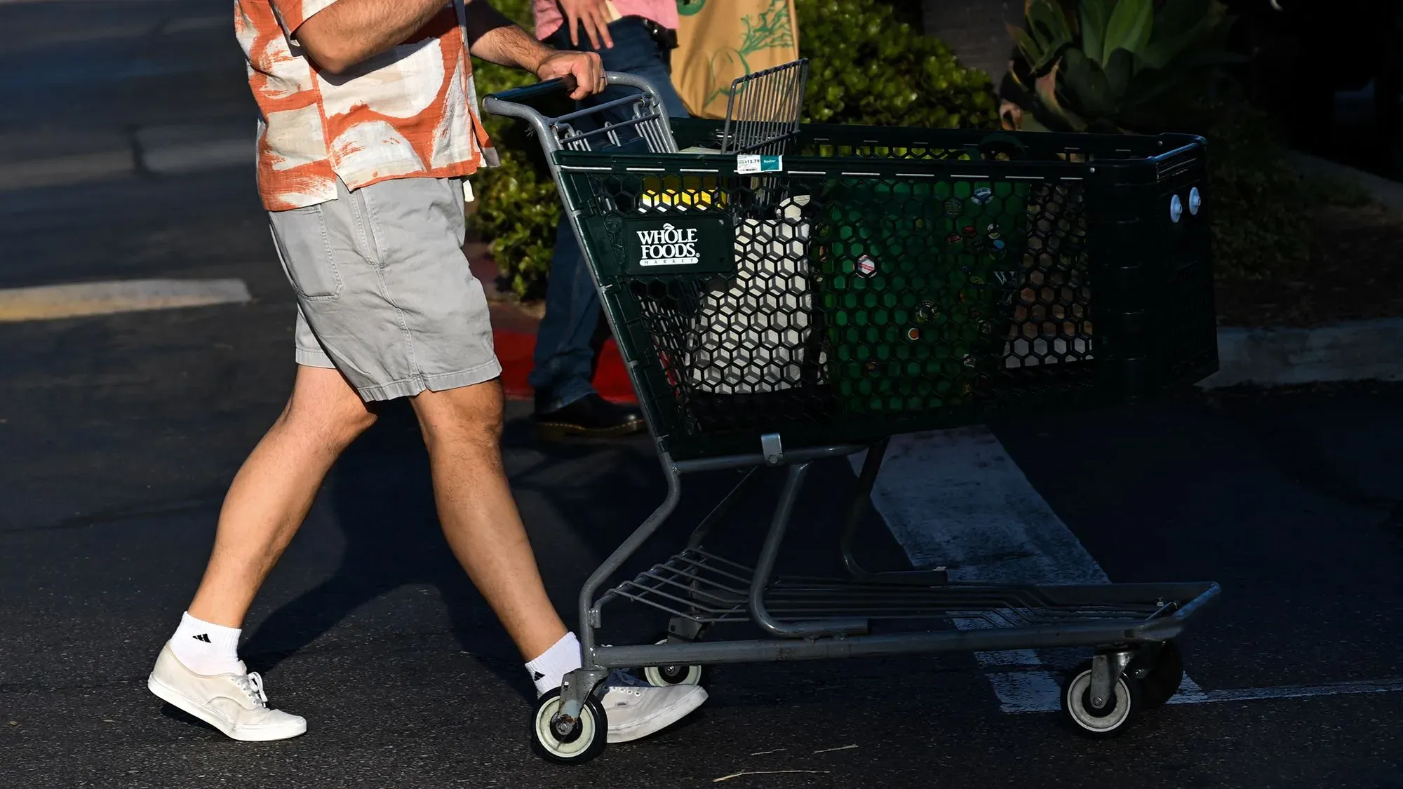 رجل يحمل عربة تسوق من متجر Whole Foods، بينما تظهر خلفه أرفف فارغة، مما يعكس تأثير الهجوم الإلكتروني على المخزون.