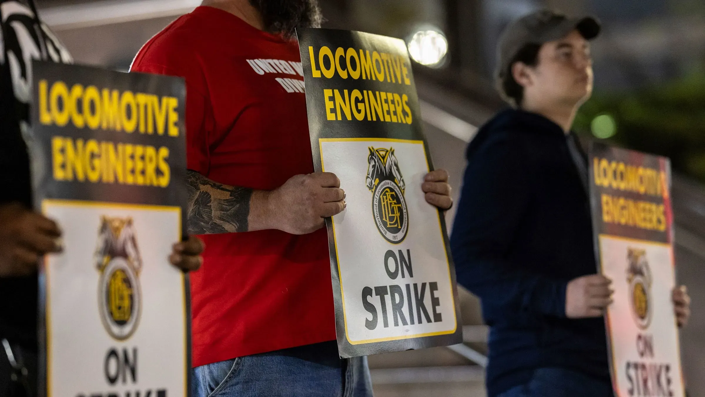 مهندسون من شركة نيوجيرسي ترانزيت يحتجون حاملين لافتات كتب عليها "مهندسو القاطرات في إضراب"، مما يعكس توقف خدمات السكك الحديدية.