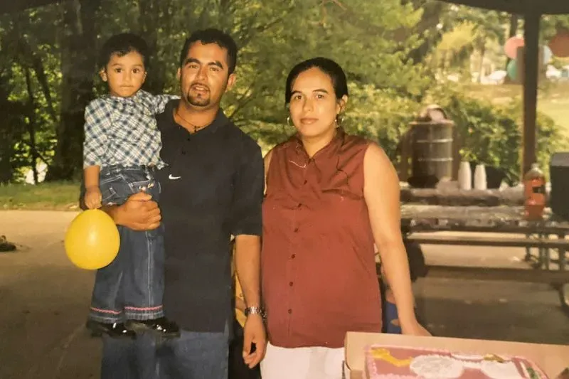 عائلة سلفادورية في حديقة، الوالد يحمل طفلاً بينما تقف الأم بجانبهما. تعكس الصورة التحديات التي تواجهها الجالية في ماريلاند.