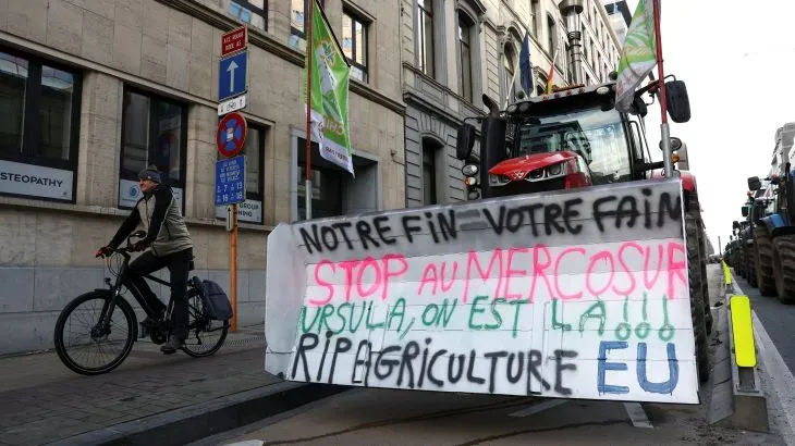 لافتة ضخمة تحمل شعارات احتجاجية ضد اتفاقية ميركوسور، مع وجود جرار زراعي في الخلفية، في بروكسل.