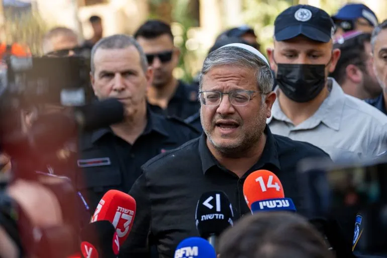 وزير الأمن القومي الإسرائيلي إيتامار بن غفير يتحدث أمام وسائل الإعلام، محاطًا بأفراد من الشرطة، وسط أجواء من التوتر السياسي.