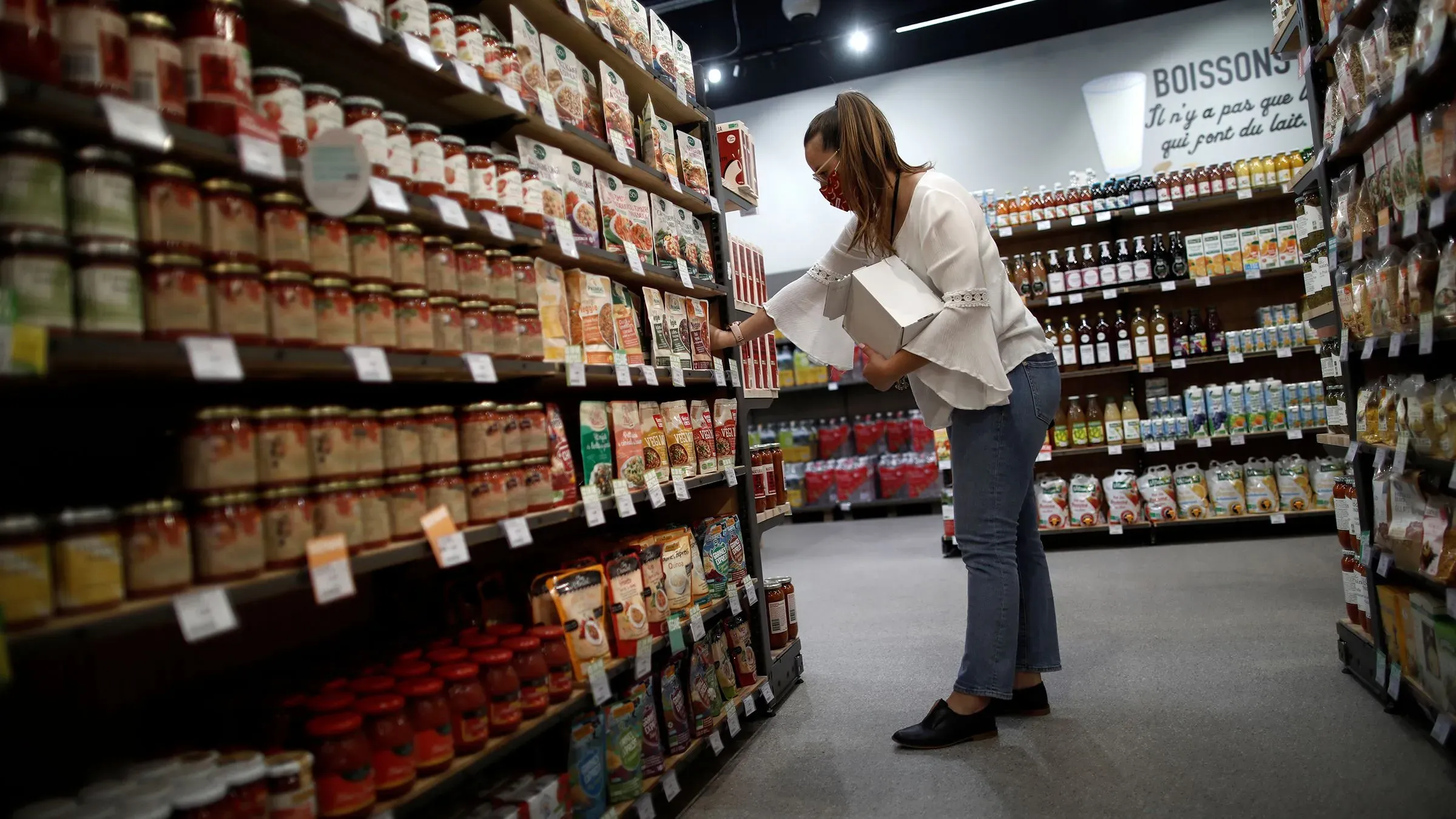 امرأة تتسوق في متجر، تختار مواد غذائية من الأرفف، تماشياً مع توجيهات المفوضية الأوروبية لتخزين الإمدادات الأساسية في حالات الطوارئ.