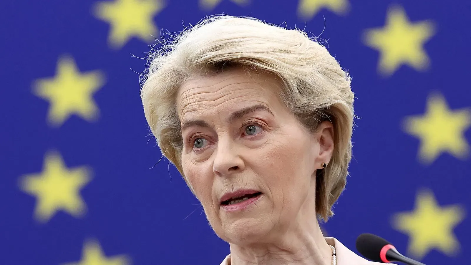 أورسولا فون دير لاين تتحدث في مؤتمر صحفي حول تأثير الرسوم الجمركية الأمريكية على الاقتصاد العالمي، مع خلفية علم الاتحاد الأوروبي.