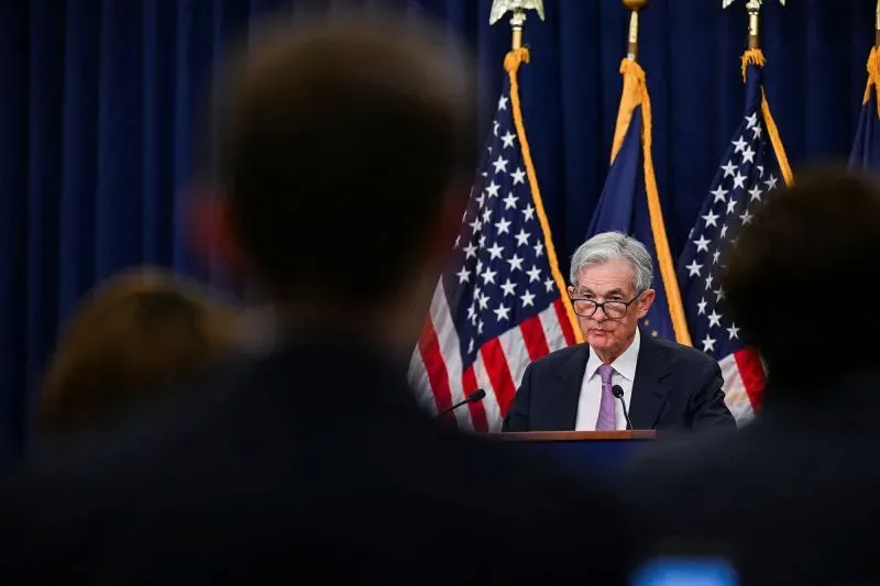 باول، رئيس الاحتياطي الفيدرالي، يتحدث في مؤتمر صحفي، مع أعلام الولايات المتحدة خلفه، وسط حالة من عدم اليقين الاقتصادي.