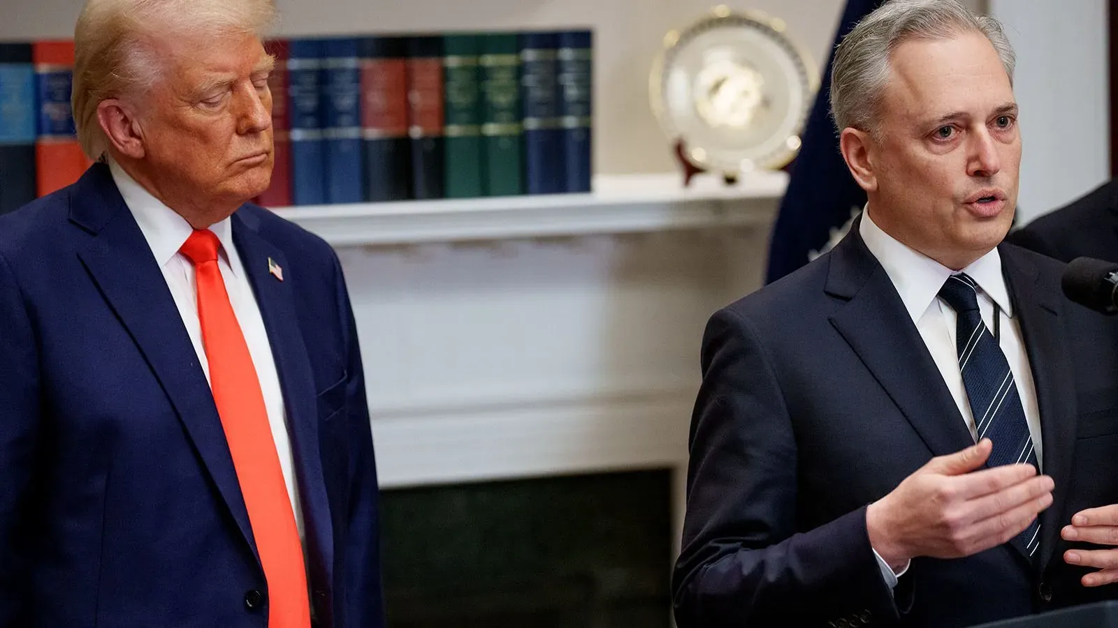 رجلان يتحدثان في مؤتمر صحفي بالبيت الأبيض، حيث يبدو الرئيس السابق ترامب مستمعًا بينما يتحدث أحد المسؤولين عن العملات الرقمية.