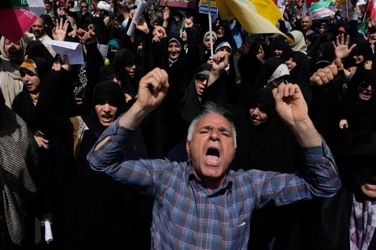 محتجون إيرانيون يرفعون الأعلام ويهتفون بشعارات قوية ضد الهجمات الأمريكية على المنشآت النووية، معبرين عن الغضب والتضامن.