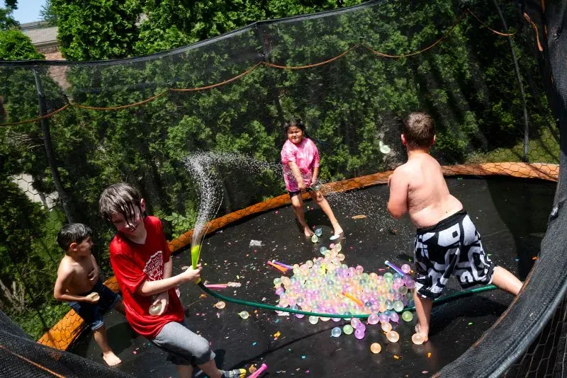 أطفال يلعبون في حديقة مع حوض قفز مائي، يتبادلون رش الماء ويستمتعون بألعاب مائية ملونة، مما يعكس لحظات من المرح والعائلة.