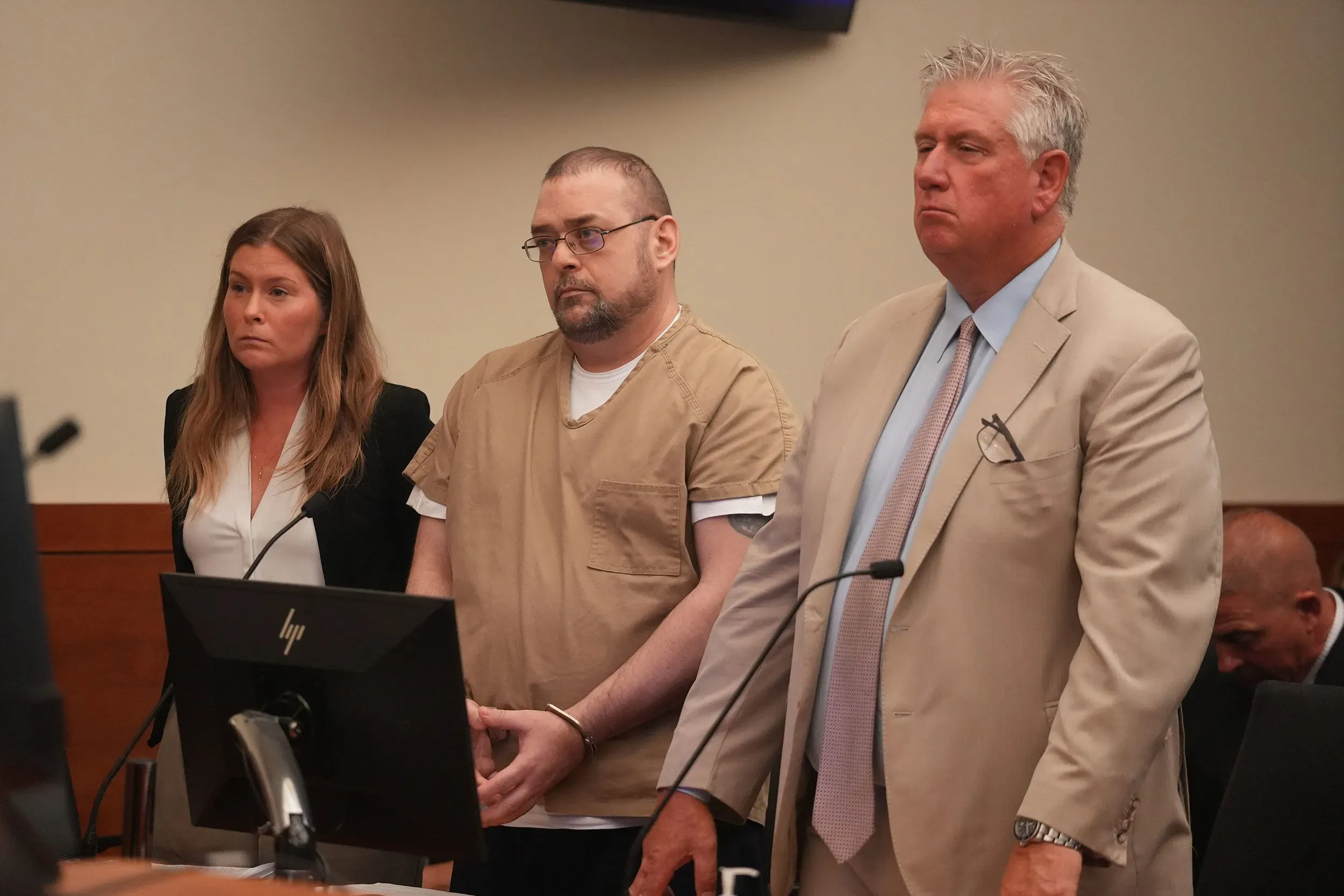 ضابط شرطة سابق يقف في المحكمة مع محاميه، حيث تم الحكم عليه بالقتل في قضية إطلاق نار على أندريه هيل، مما أثار جدلاً حول استخدام القوة من قبل الشرطة.