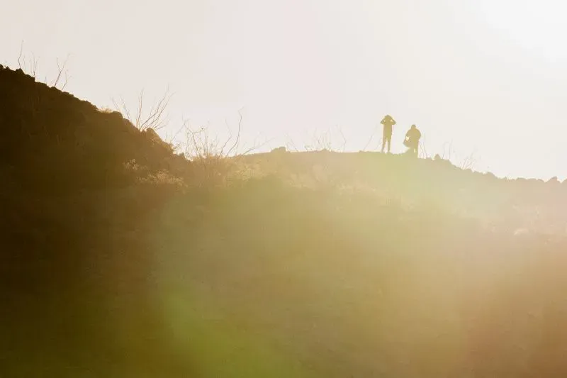 صورة تظهر شخصين على قمة تلة، يستعدان لمراقبة الطائرات بدون طيار MQ-9 التي تحلق فوق المكسيك في سياق مكافحة المخدرات.