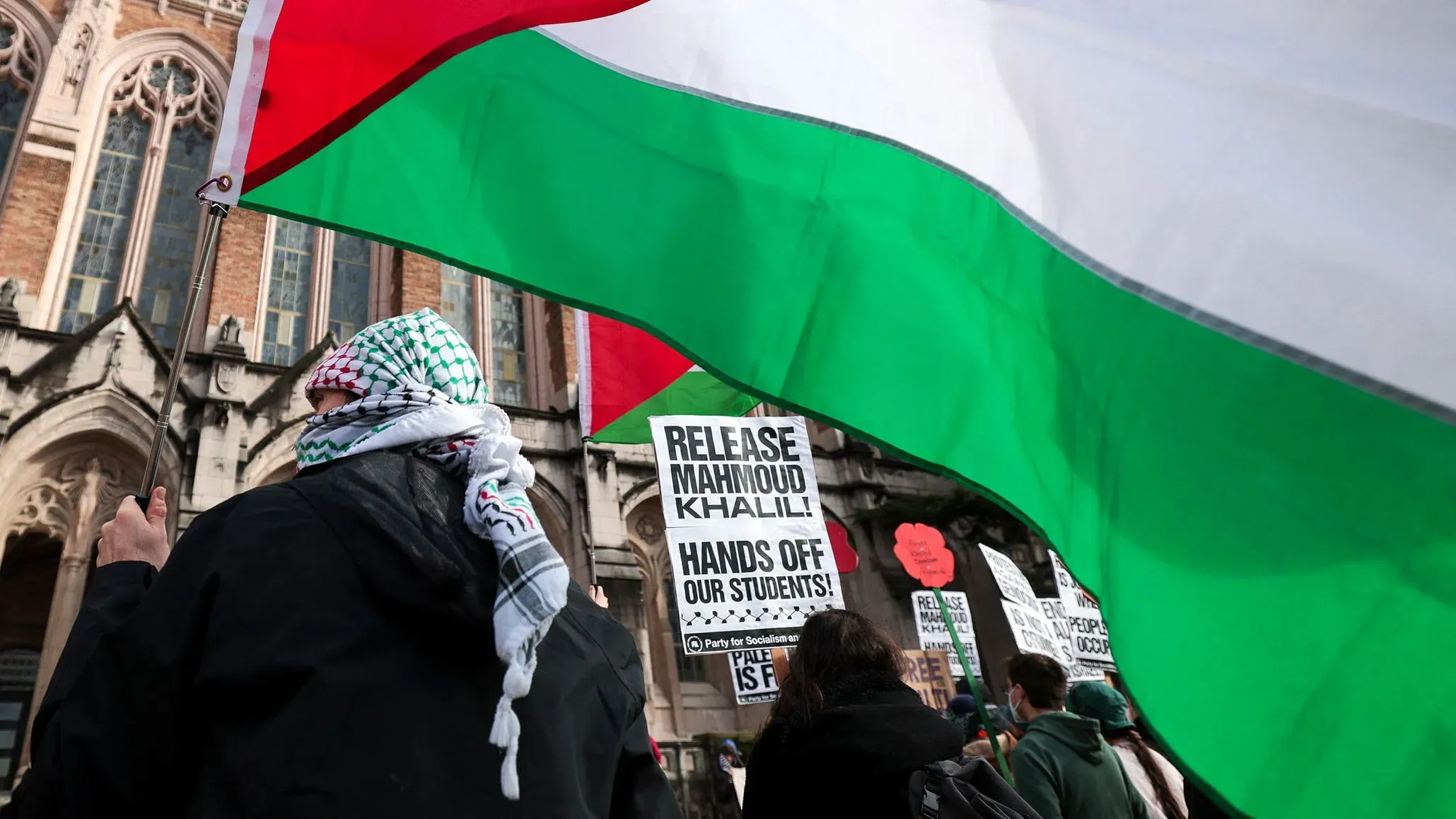 تجمع حاشد لدعم الناشط محمود خليل، حيث يحمل المتظاهرون لافتات تطالب بالإفراج عنه، مع العلم الفلسطيني في الخلفية.