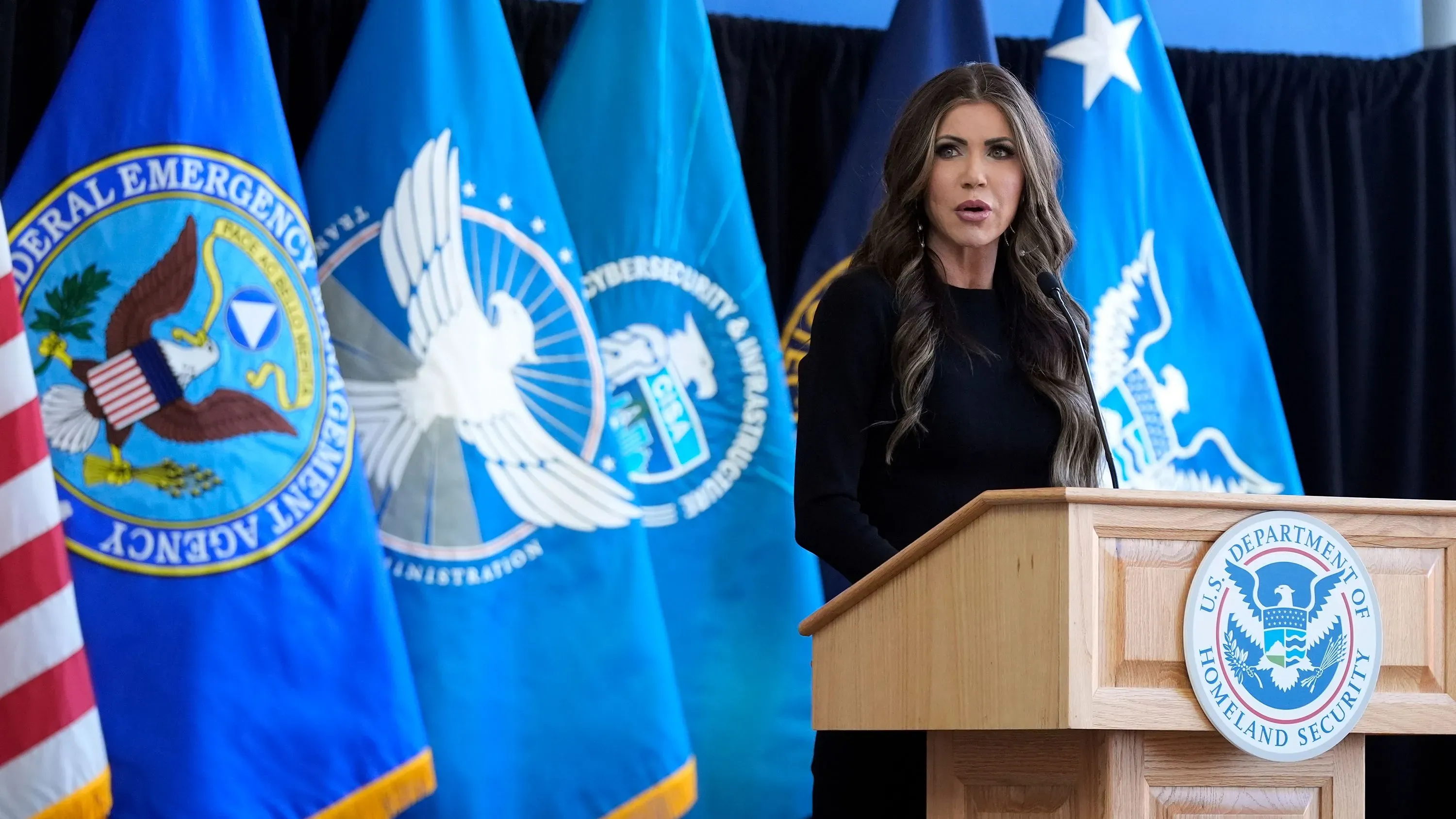 وزيرة الأمن الداخلي كريستي نويم تتحدث في مؤتمر صحفي، مع وجود أعلام الوكالة الفيدرالية لإدارة الطوارئ في الخلفية.