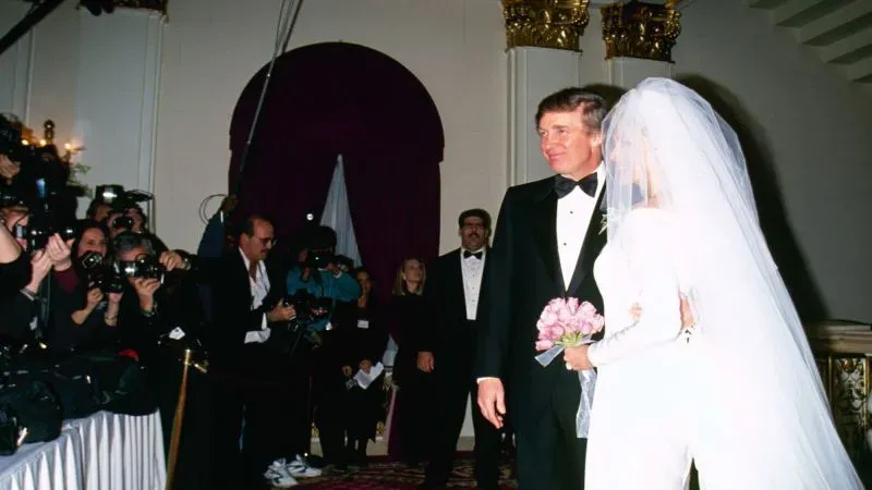 عروس وعريس في حفل زفاف ترامب عام 1993، مع وجود مصورين في الخلفية، حيث ترتدي العروس فستانًا أبيض.
