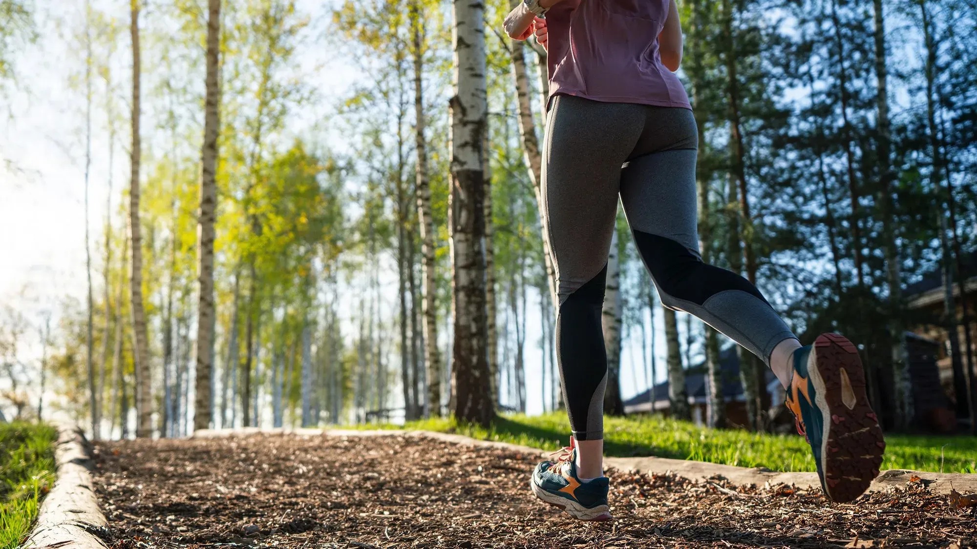 امرأة تجري على ممر محاط بالأشجار، تعكس الصورة أهمية النشاط البدني في تحقيق الصحة والعافية.