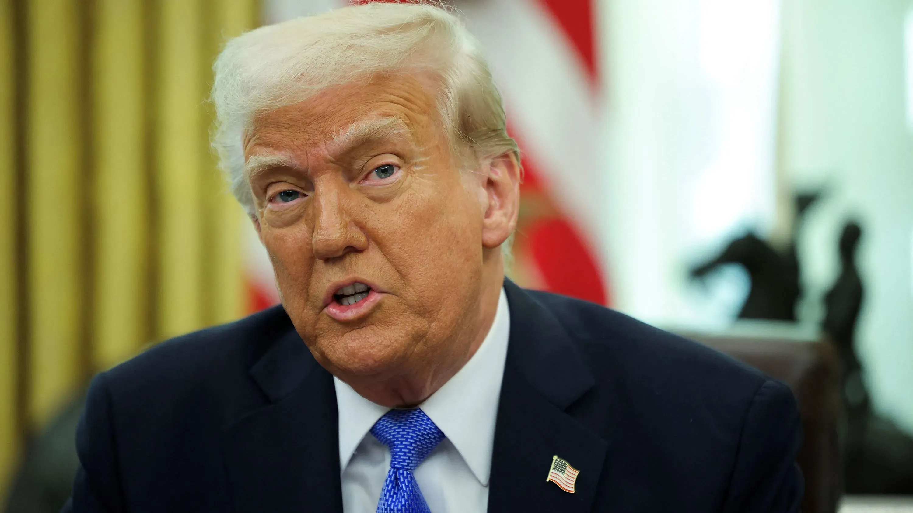 ترامب يتحدث في المكتب البيضاوي، مع التركيز على ادعاءاته حول الانتخابات والعجز التجاري، وسط خلفية علم الولايات المتحدة.