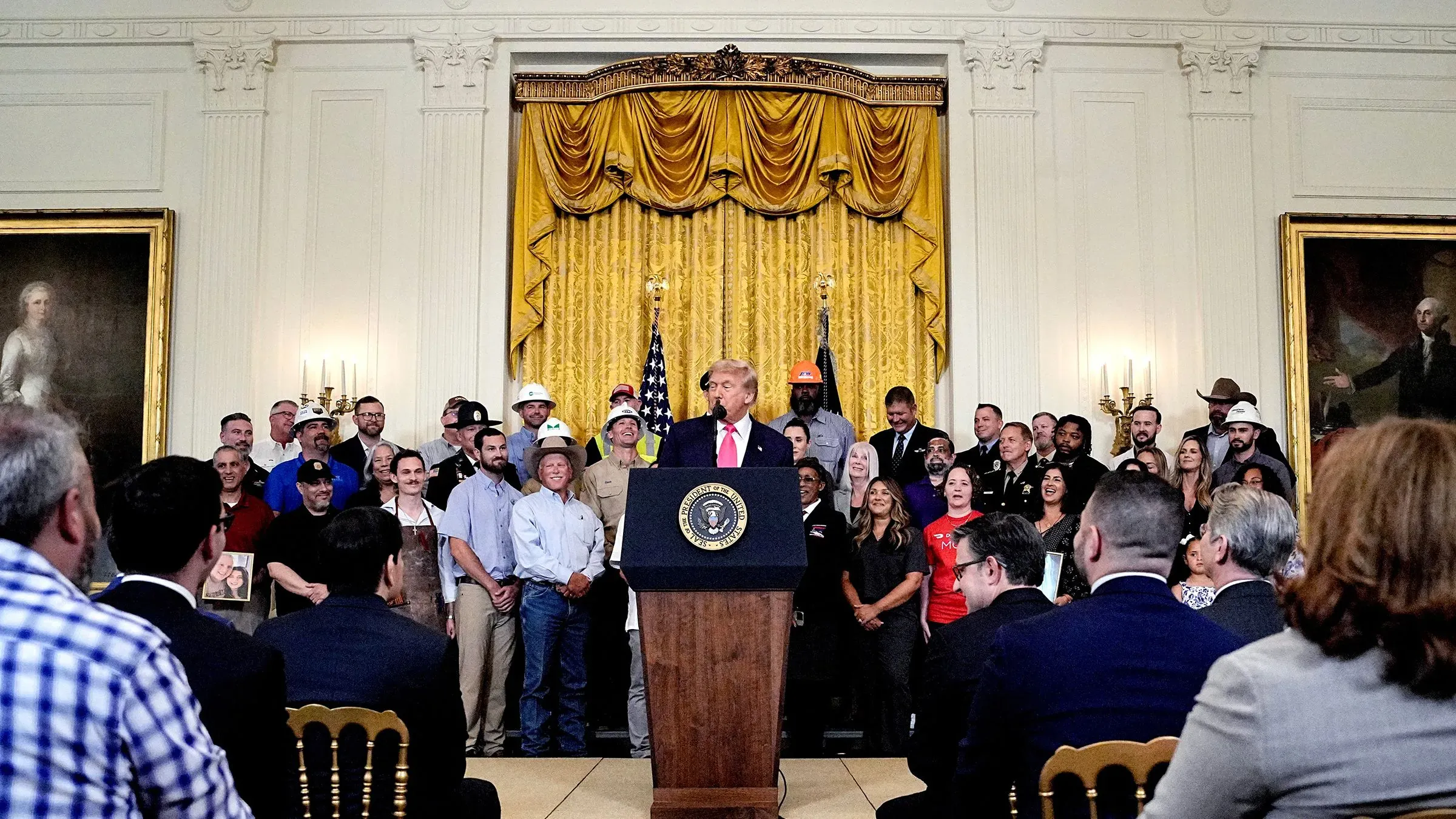 ترامب يتحدث في البيت الأبيض أمام حشد من الناس، مع وجود علم أمريكي خلفه، أثناء مناقشة مشروع قانون السياسة الداخلية.