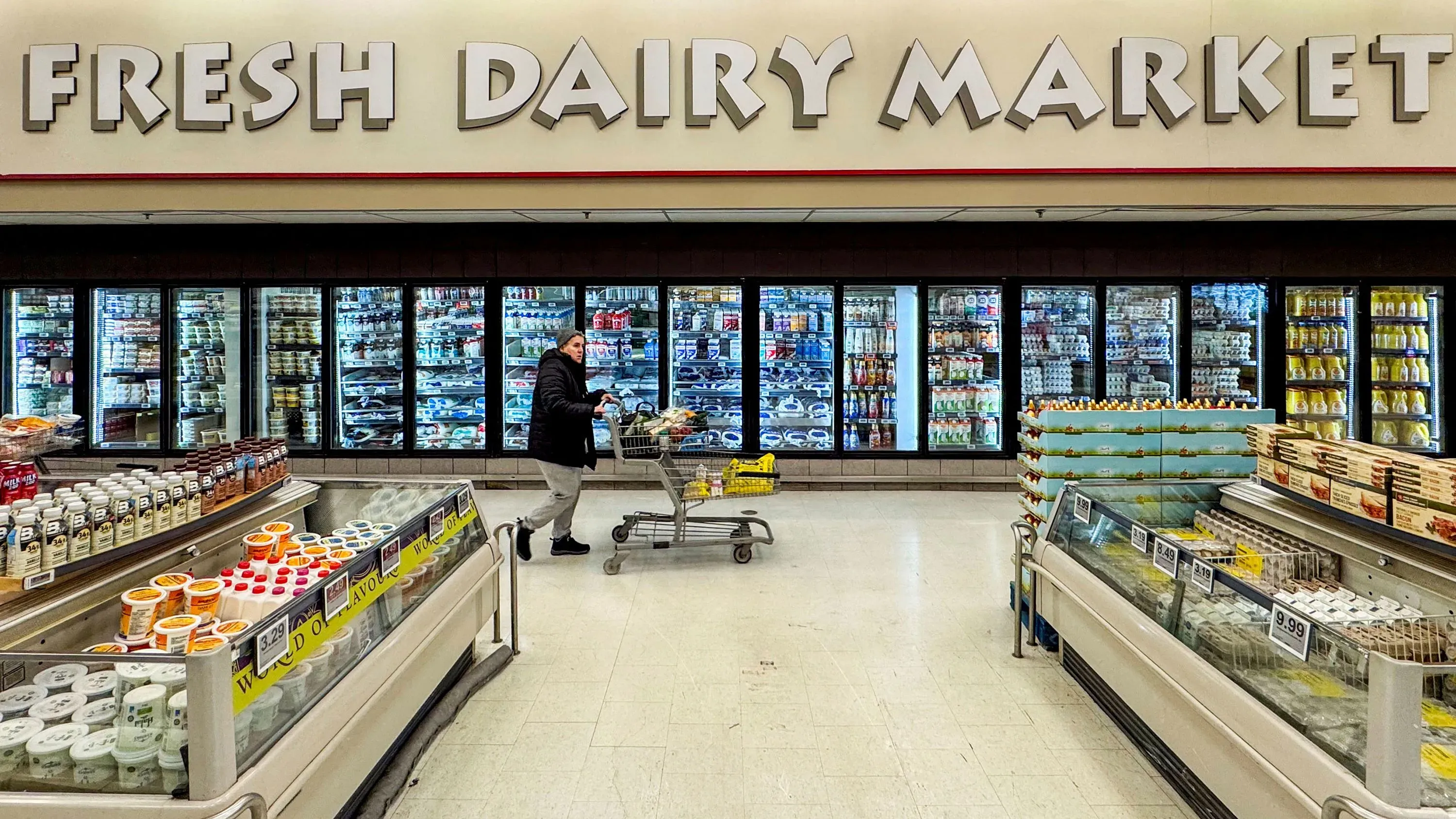 سوق الألبان الطازجة في سوبرماركت، حيث تظهر امرأة تدفع عربة تسوق أمام رفوف مليئة بمنتجات الألبان المختلفة.