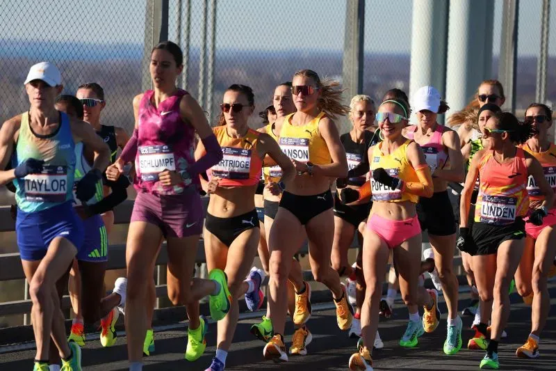 مجموعة من العدائين الإناث يشاركن في سباق، يرتدين ملابس رياضية ملونة، ويظهرن حماسهن أثناء الجري في بيئة خارجية.