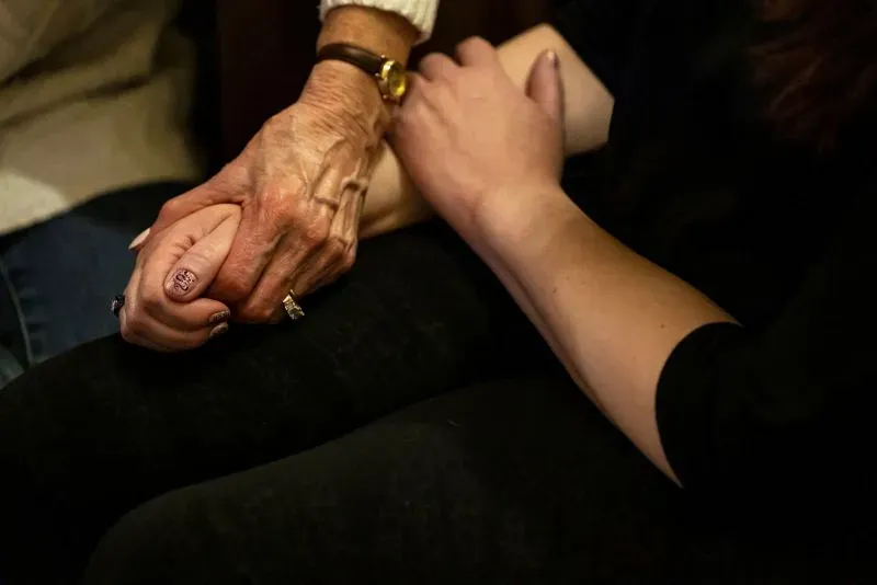 يدينان متشابكتان، تمثلان علاقة الدعم بين سو وآن ماري، حيث تعكسان التعافي من مأساة كولومباين.