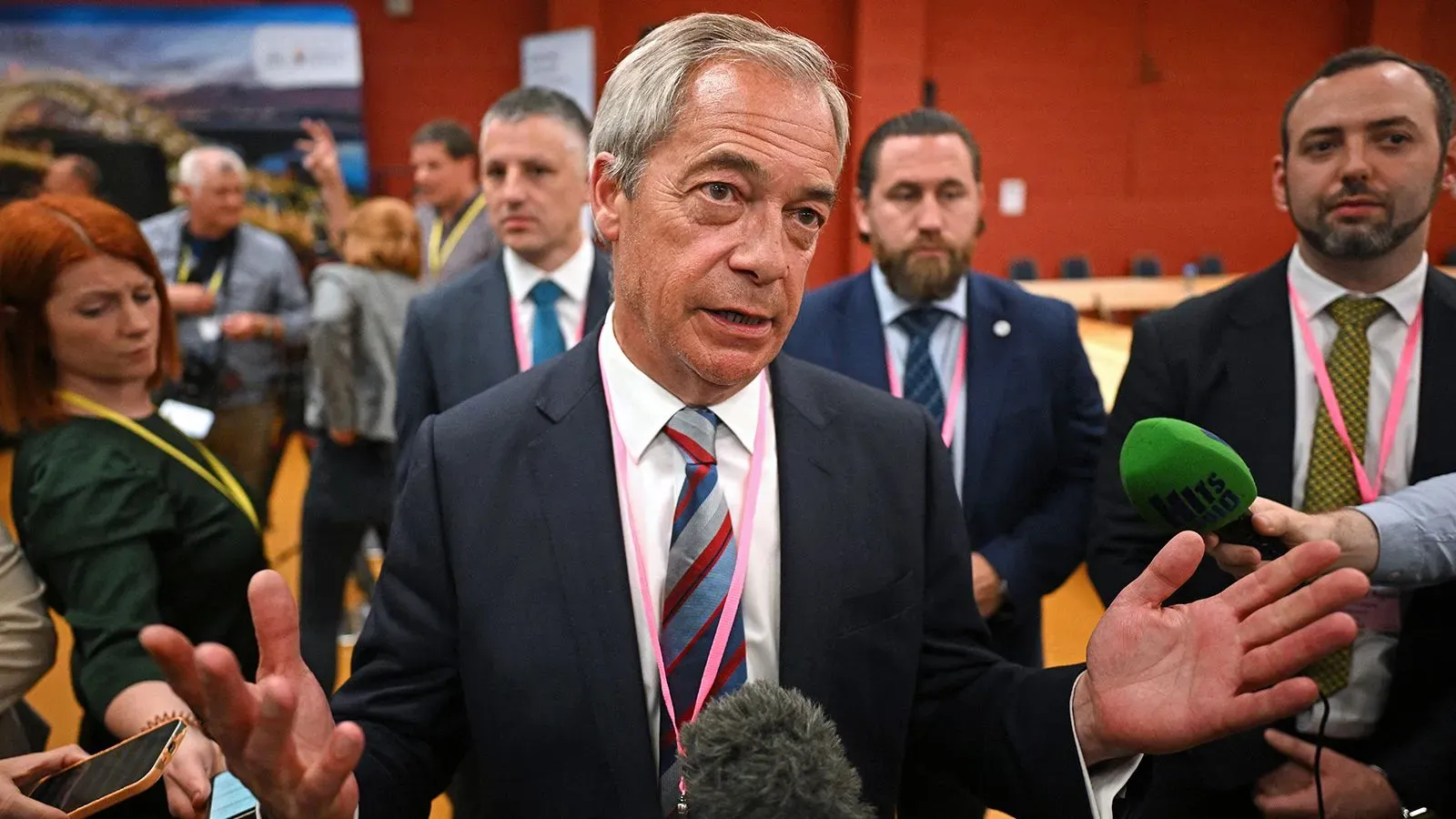 نايجل فاراج يتحدث في مؤتمر صحفي بعد فوز حزبه "الإصلاح البريطاني" بمقعد في البرلمان، محاطًا بمؤيدين وصحفيين.