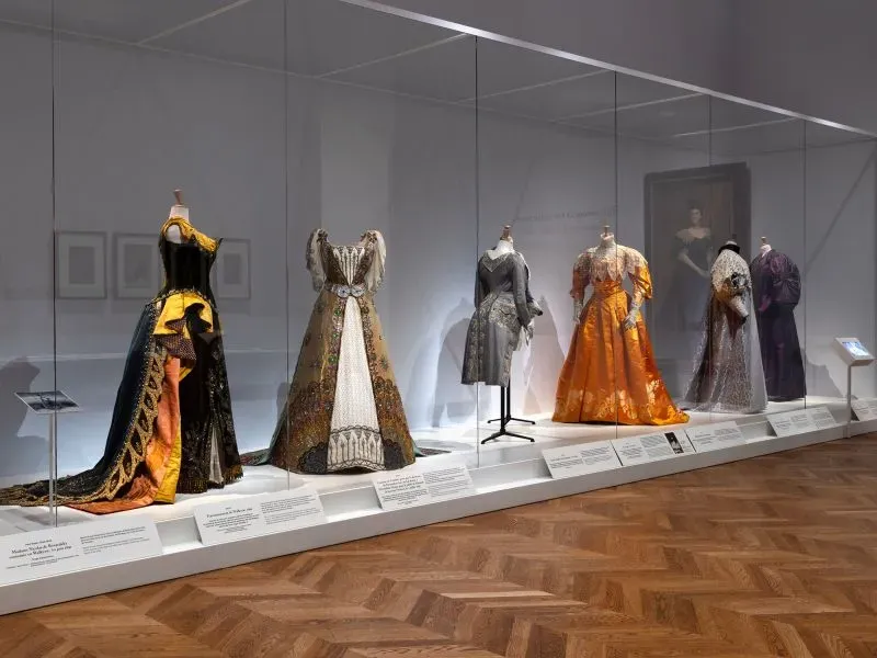 عرض لفساتين تاريخية مصممة من قبل تشارلز فريدريك وورث، تُظهر تأثيره في عالم الأزياء الراقية، ضمن معرض في متحف بيتي باليه في باريس.