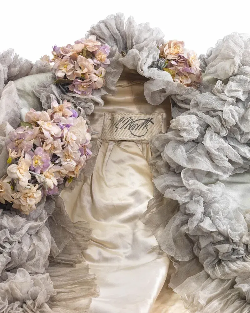 فستان تاريخي من تصميم تشارلز فريدريك وورث، مزين بأزهار ملونة وطبقات من القماش، يعكس إرث الأزياء الراقية.